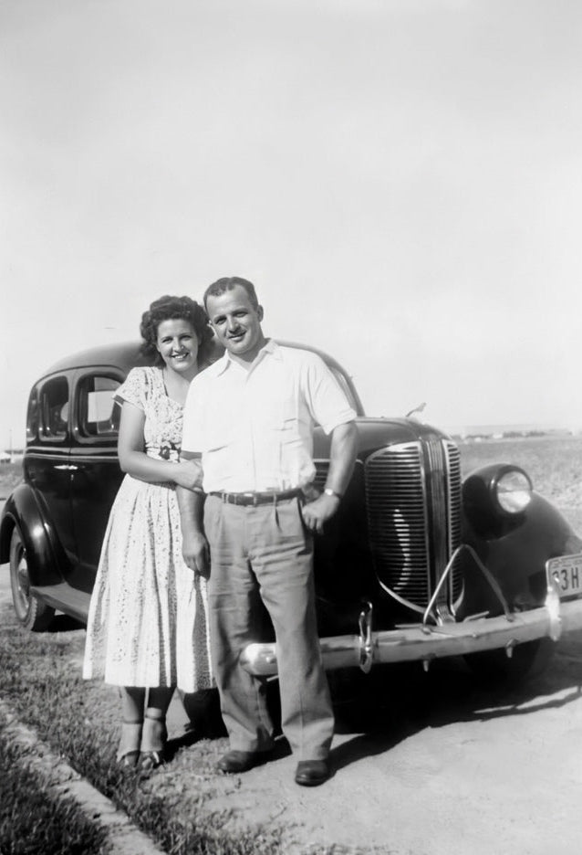 Black and white photo of a Marie and Dominick Pizzio standing next to an old car on a road.